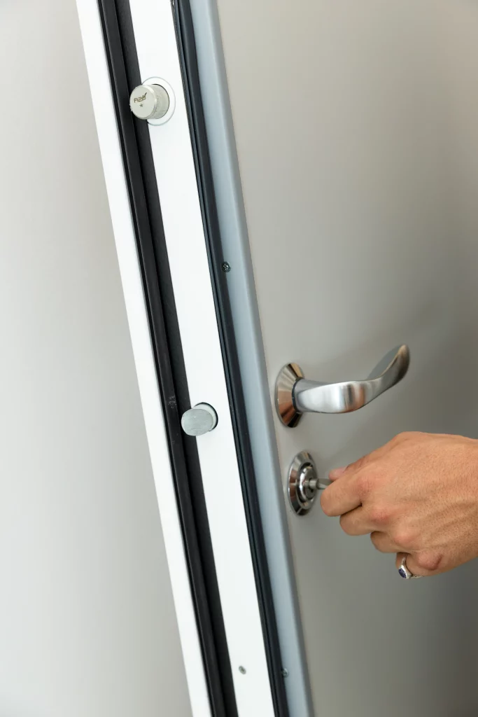 Gros plan sur les points de verrouillage d'une porte blindée, poignée chromée et main insérant la clé dans le cylindre