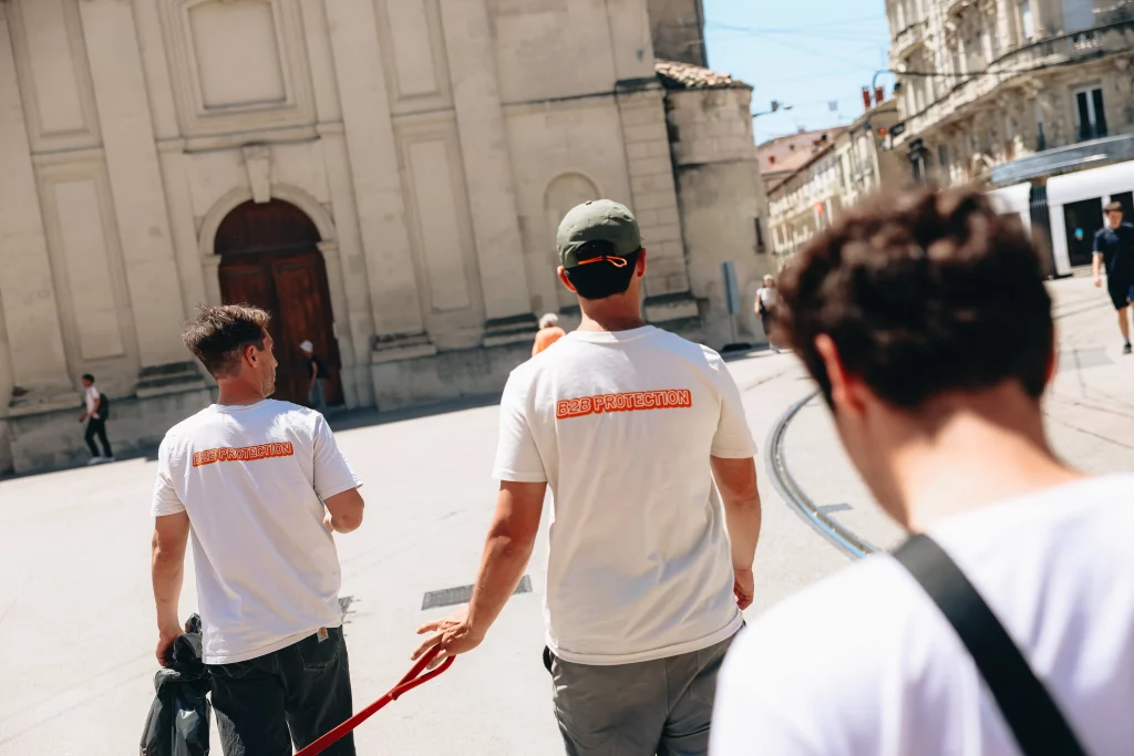 Trois membres de l'équipe B2B Protection, t-shirts floqués, marchant sur une place historique avec le tramway en arrière-plan